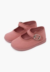 Zapatos Mary Jane de lona rosa con punta redondeada, correa ajustable y acento de hebilla metálica. Suela plana de goma y detalles cosidos en los bordes.