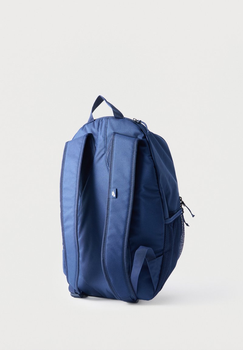 Blauer Rucksack mit gepolsterten Schultergurten, Tragegriff oben und seitlicher Netztasche, aufrecht stehend vor hellem, einfarbigem Hintergrund.