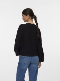 Črni pleteni pulover z udobnim krojem, rebrasto teksturo in balonastimi rokavi, kombiniran s svetlo modrimi jeans hlačami v sproščenem zadnjem pogledu.