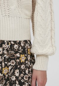 Maglione a maglia di crema testurizzata con polsini larghi e gonna floreale nera a fantasia con fiori gialli e bianchi su strisce verticali.