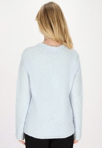 Pulover bleu deschis, pufos, cu guler rotund și mâneci lungi. Textura este moale și pufoasă, având o croială lejeră într-o culoare uniformă.