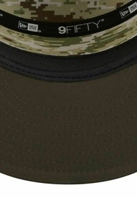 Camouflage cap with a wide brim, featuring a textured fabric in greens and browns. Black accents on the underside and inner band.