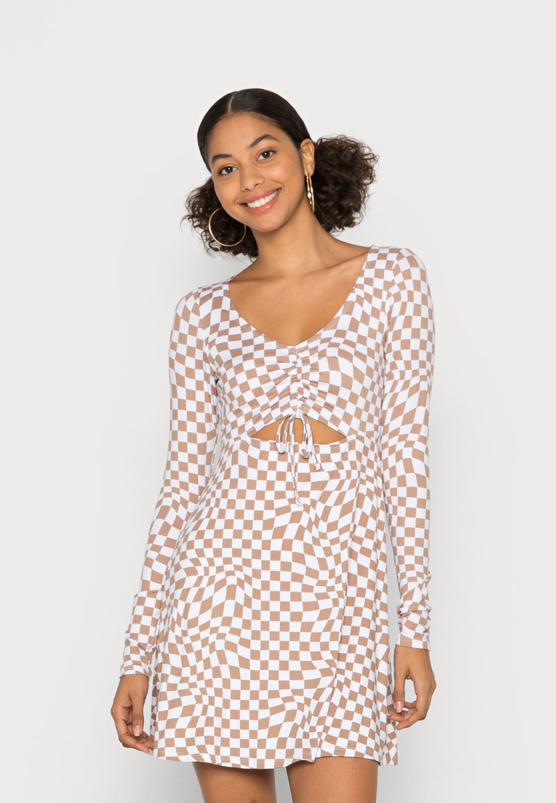 Vestido mini de mangas longas em padrão xadrez castanho e branco, apresentando um detalhe franzido à frente com um laço e um recorte na cintura.