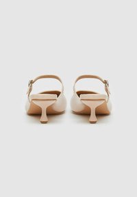 Sandales en cuir beige à talon carré avec une sangle arrière à la cheville et une boucle décorative. Bout rond et forme unique du talon.