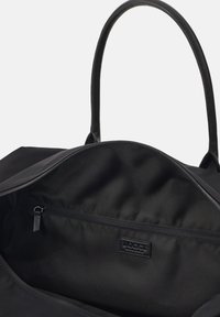 Svart tote-väska med släta läderhandtag, dragkedjeslutning och en rymlig insida som har ett litet dragkedjefack och logotypdetalj.