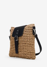 Bolso cruzado de paja tejido con solapa y correa de cuero negro, que presenta una forma rectangular y un exterior texturizado. Incluye detalles metálicos en plata.