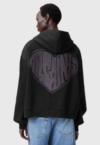 Felpa nera con design oversize, caratterizzata da un logo a forma di cuore di un profondo viola. Tessuto morbido con vestibilità rilassata e polsini a costine.