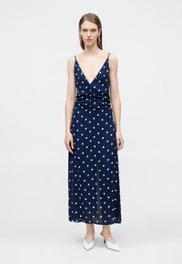 Μάξι φόρεμα σε ναυτικό μπλε με πουά σχέδιο, βαθύ ντεκολτέ και λεπτομέρεια συγκέντρωσης στη μέση. Λείο ύφασμα, λεπτές τιράντες και ανοίγματα στο πλάι.