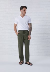 T-shirt bianco a scollo a V abbinato a pantaloni con coulisse verde oliva e sandali neri. Tessuto morbido con una vestibilità comoda e tasche laterali.