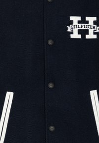 Námornícky modrá varsity bunda z vlnenej zmesi s bielymi pruhmi, cvokmi a vyšitým logom s nápisom "HILFIGER."