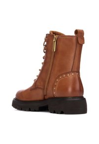 Botín de cuero marrón hasta el tobillo con cordones en la parte delantera, cremallera lateral, acentos de tachuelas y suela negra gruesa. Superficie texturizada con costuras reforzadas.