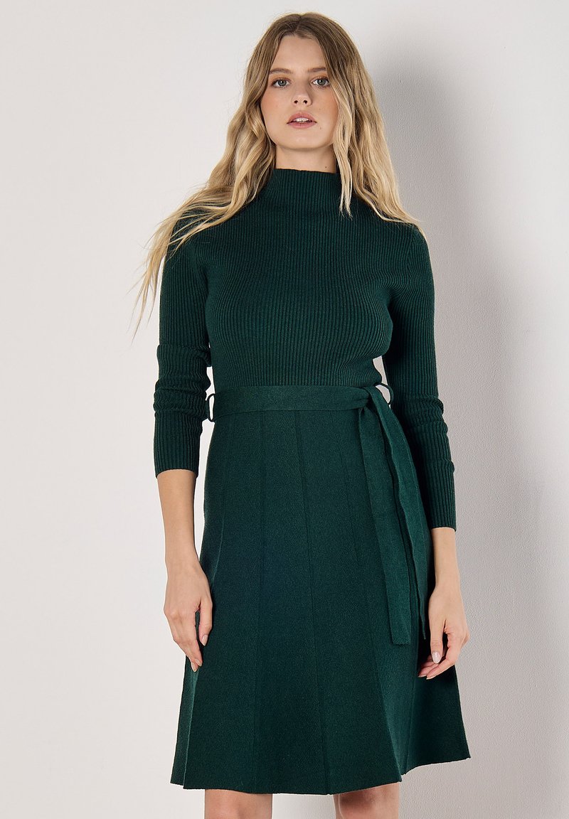 Robe en tricot verte avec un col haut, des manches longues, une ceinture à la taille et une jupe évasée. Présente une texture côtelée et une finition lisse.