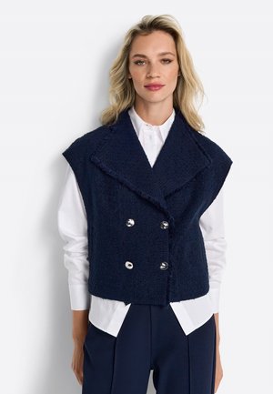 Navy blue double-breasted vest with large silver buttons, featuring a textured fabric and wide lapels. Worn over a white shirt.