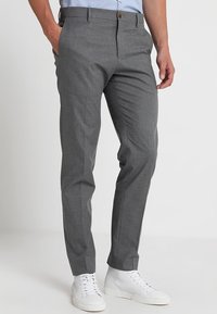 Pantaloni grigi su misura realizzati in un tessuto testurizzato, con una linea dritta, passanti per la cintura e chiusura frontale con bottone, abbinati a sneakers bianche.