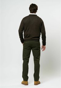 Rjav pleten pulover, zeleni chinoski hlače in peščene čevlje. Pulover ima okroglo ovratnik in rebraste manšete; chinoski hlače imajo dve zadnji žepu s gumbi.