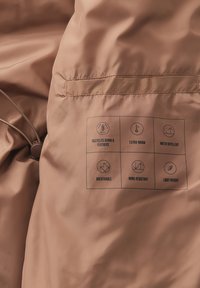 Recycelte Daunen- und Federjacke in einem matten hellbraunen Finish. Verfügt über Etiketten für zusätzliche Wärme, Wasserabweisung, Atmungsaktivität und Windbeständigkeit.