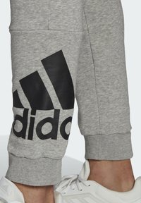 Szare dresy z czarnym logo Adidas i wzorem trzech pasków. Ściągacze na kostkach. Materiał bawełniany z gładką teksturą.