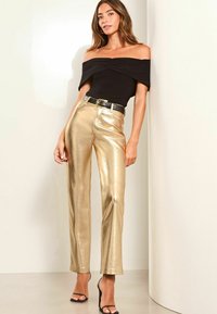 Melna topiņa bez Piedurknēm ar ruchešanu, savienota ar spīdīgām zeltītām augsto jostasvietu biksēm un melnu jostu. Melna siksnīšu augstpapēžu kurpes noslēdz izskatu.