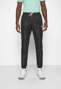 Zwarte sportieve broek met een elastische tailleband en witte koord, voorzien van een zijlogo en een taps toelopende pasvorm bij de enkels.