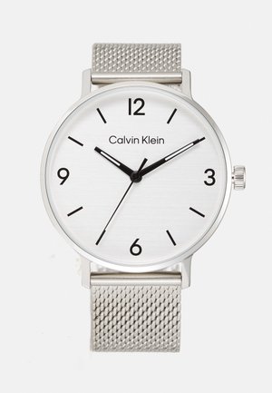Silver stainless steel watch with a round brushed white dial, black hour markers, and mesh strap. Features brand name at 12 o'clock and a crown.