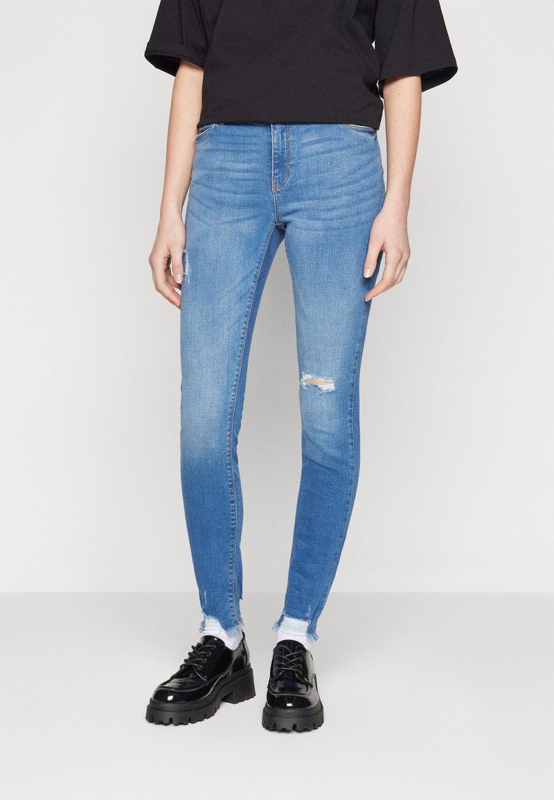 Modre skinny jeans iz denima, z raztrganimi koleni in strgani robovi. V kombinaciji s črnimi lakastimi platform čevlji.