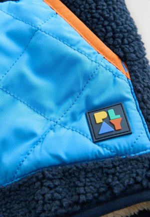 Tessuto blu trapuntato con rifiniture arancioni e fleece nero testurizzato; presenta un logo colorato con forme geometriche.