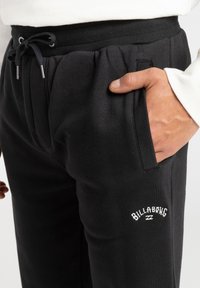 Black sweatpants made of soft material, featuring a drawstring waistband, side pockets, and a white embroidered Billabong logo.