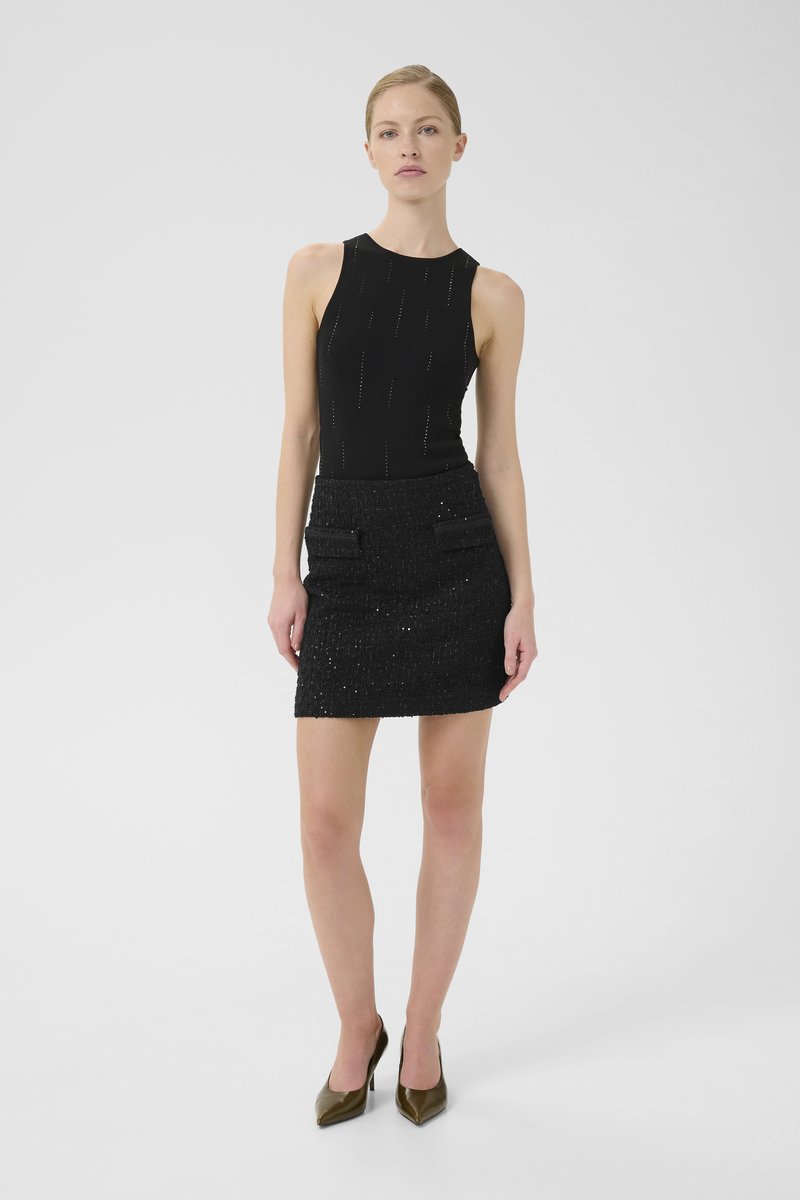 Schwarzes ärmelloses Oberteil mit vertikaler Naht; kombiniert mit einem strukturierten schwarzen Minirock, der zwei vordere Klappentaschen aufweist.