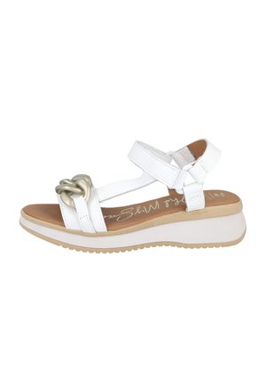 Sandalia de cuero blanco con plantilla en tono marrón claro, suela de cuña baja, tira en el tobillo y hebilla metálica decorativa torcida en la tira delantera.