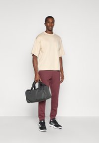 Látkový béžový oversized tričko, bordové zúžené nohavice, čierne tenisky, šedá športová taška. Jednoduchý dizajn s krátkymi rukávmi a bez vzorov.