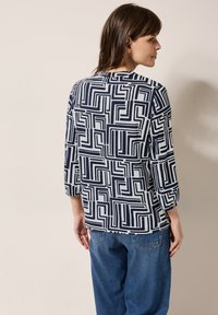 Blusa de rayas en azul marino y blanco con mangas tres cuartos, que presenta formas geométricas y un corte holgado. La tela es suave y ligera.