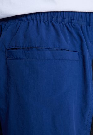Marineblaue Sportshorts mit elastischem Bund und einer Gesäßtasche mit gestepptem Rand. Der Stoff hat eine leicht strukturierte Oberfläche.