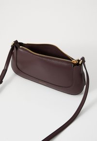 Dunkelburgunderfarbene Lederhandtasche mit glatter Textur, goldenem Reißverschluss, einem einzelnen Schulterriemen und einem dezenten Logo an der Seite.