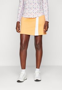 Falda de tenis amarilla con un panel lateral blanco, hecha de una tela suave y ligera. Combinada con zapatillas deportivas y calcetas blancas para el deporte.