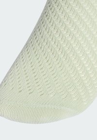 Svetlozelená pletená ponožka s texturovaným vzorom a rebrovaným lemom. Má hladkú oblasť na prstoch a jemné detaily po celej ponožke.