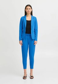 Sinine bleiser ja sobivad joggerid siledast kangast, mis on slim-fit lõikega, tõmbluku ja musta tank-topiga all. Rihmadega mustad sandaalid.