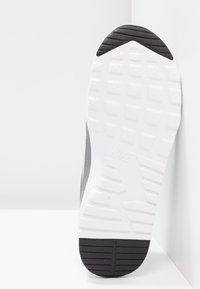 Sneaker Nike avec une tige grise texturée, semelle blanche présentant des motifs de traction, et un logo en relief au niveau du talon. Design à profil bas.