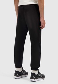 Zwarte sweatpants gemaakt van soepel materiaal met elastische boorden. Heeft een relaxte pasvorm en een eenvoudig ontwerp. Draagt met zwarte sneakers en witte sokken.
