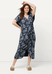 Laivansinis maxi-mekko, jossa on paisley-kuvio; väljä malli, V-pääntie ja lyhyet hihat. Sivussa halkio, yhdistetty valkoisten korkokenkien kanssa.