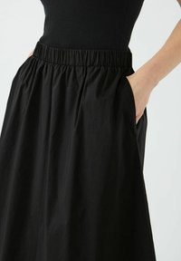 Jupe noire avec une ceinture élastique et des poches latérales, présentant une texture lisse et un design ample et fluide.
