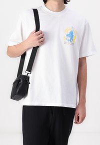 Vit bomull t-shirt med färggrafisk tryck på bröstet. Svart mini-väska i läder med dragkedjestängning och justerbar axelrem.