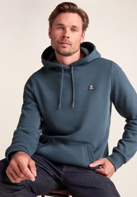 Blue hoodie with a front pocket, drawstring hood, and small logo on the chest. Material appears soft and textured.