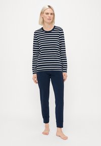 Marineblauw en crème gestreepte longsleeve top gecombineerd met effen marineblauwe broek. Beide gemaakt van zachte stof, met een ontspannen pasvorm en elastische manchetten.