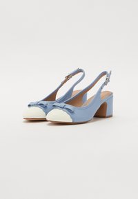 Blå slingback-sko med hvit avrundet tå, bølgekant og sløyfe-detalj på fronten. Har en solid blokkhæl og glatt tekstur.