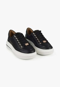 Zwarte leren sneakers met een witte middenzool, voorzien van zwarte veters en een metallic detail op de tong. Gestructureerde achterkant voor extra detail.