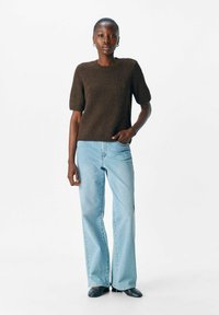 Bruin gebreid t-shirt met korte mouwen en een ronde halslijn, gecombineerd met lichtblauwe flared jeans en zwarte puntige schoenen.