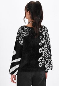 Maglione a righe bianche e nere con una texture soffice, caratterizzato da audaci design a leopardo e astratti sulle maniche e sul retro.
