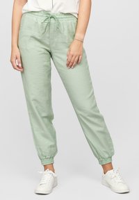 Pantalon de jogging vert clair avec taille élastique, à fermeture à cordon, poches et bas de jambes fuselés. Porté avec des baskets blanches.