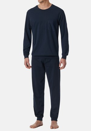 Man draagt een donkerblauw shirt met lange mouwen met dunne verticale strepen en bijpassende donkerblauwe broek, staat op blote voeten op een witte achtergrond.