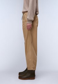 Beige bukse med elastisk midje, sidelommer og rett snitt, kombinert med mørkegrønne anklestøvler med teksturert lær og gummisåle.